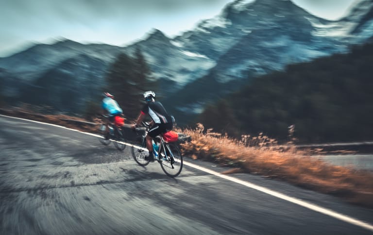Deux cyclistes roulent au pied d’un massif montagneux.
